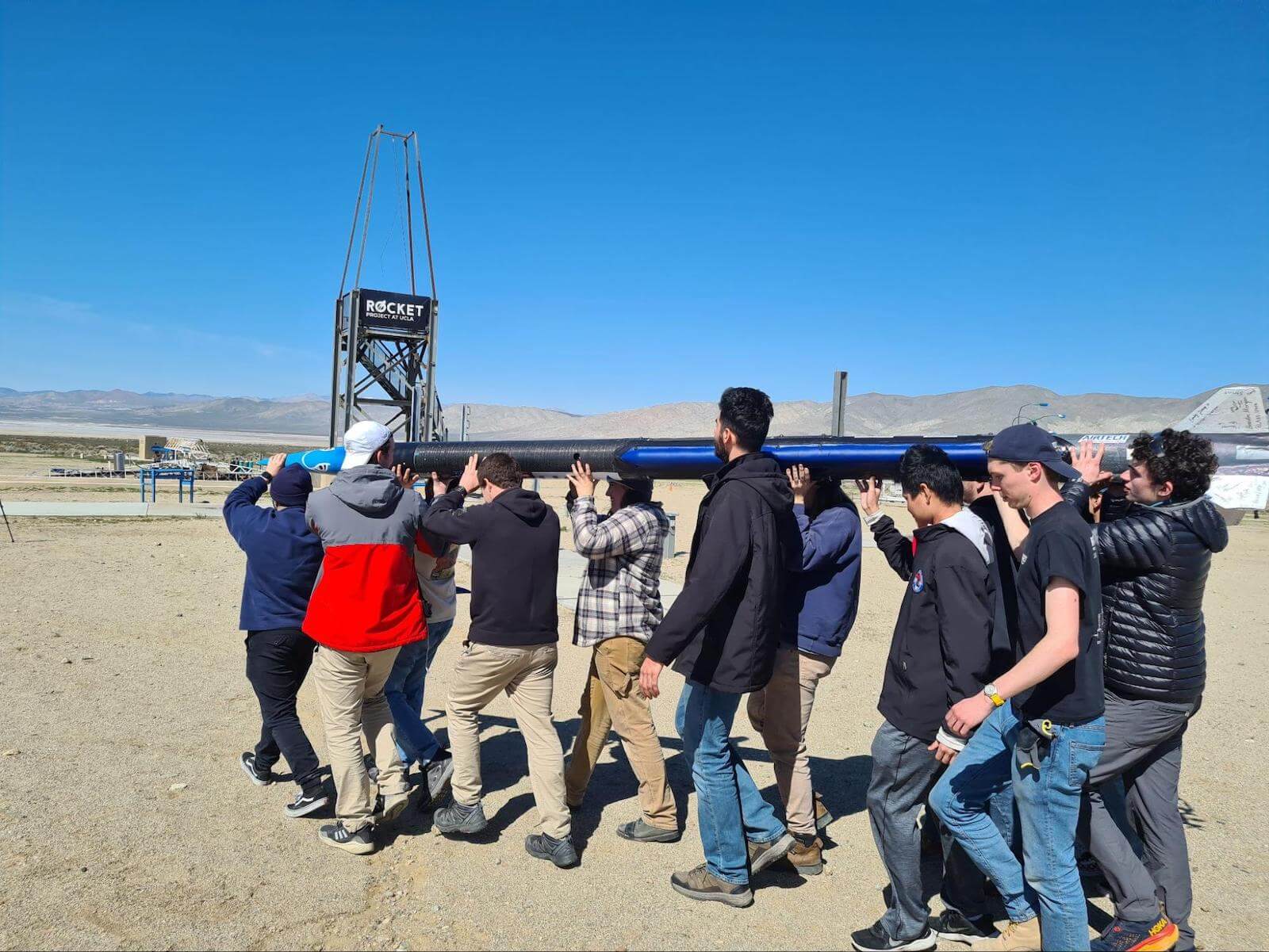 A photo of a group of people in the desert carrying a large rocket.
